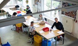 Mehrere Mitarbeiter der Caritas Werkstatt für Menschen mit Behinderung München sitzen an einem Tisch und lachen in die Kamera | © Caritas Werkstatt für Menschen mit Behinderung München