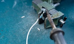 Ein Kabel wird an ein Produkt aus Eisen gelötet | © Caritas Werkstatt für Menschen mit Behinderung München