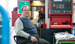 Ein Mitarbeiter der Caritas Werkstatt für Menschen mit Behinderung München sitzt mit einem Gerät in der Hand vor einer Maschine | © Caritas Werkstatt für Menschen mit Behinderung München