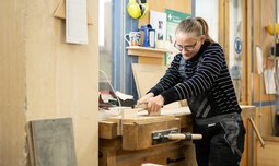Eine Mitarbeiterin der Caritas Werkstatt für Menschen mit Behinderung München steht in der Schreinerei und bearbeitet ein Holzprodukt | © Caritas Werkstatt für Menschen mit Behinderung München