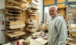Ein Mitarbeiter der Caritas Werkstatt für Menschen mit Behinderung München steht vor mehreren Holzteilen und heilt eines davon in der Hand | © Caritas Werkstatt für Menschen mit Behinderung München